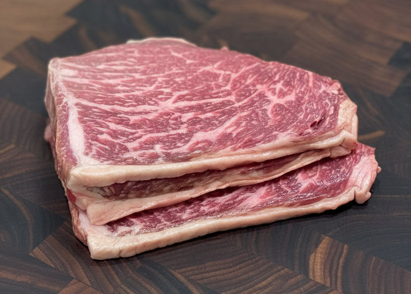 Stack of three raw, pink Wagyu minute steaks on a chopping board