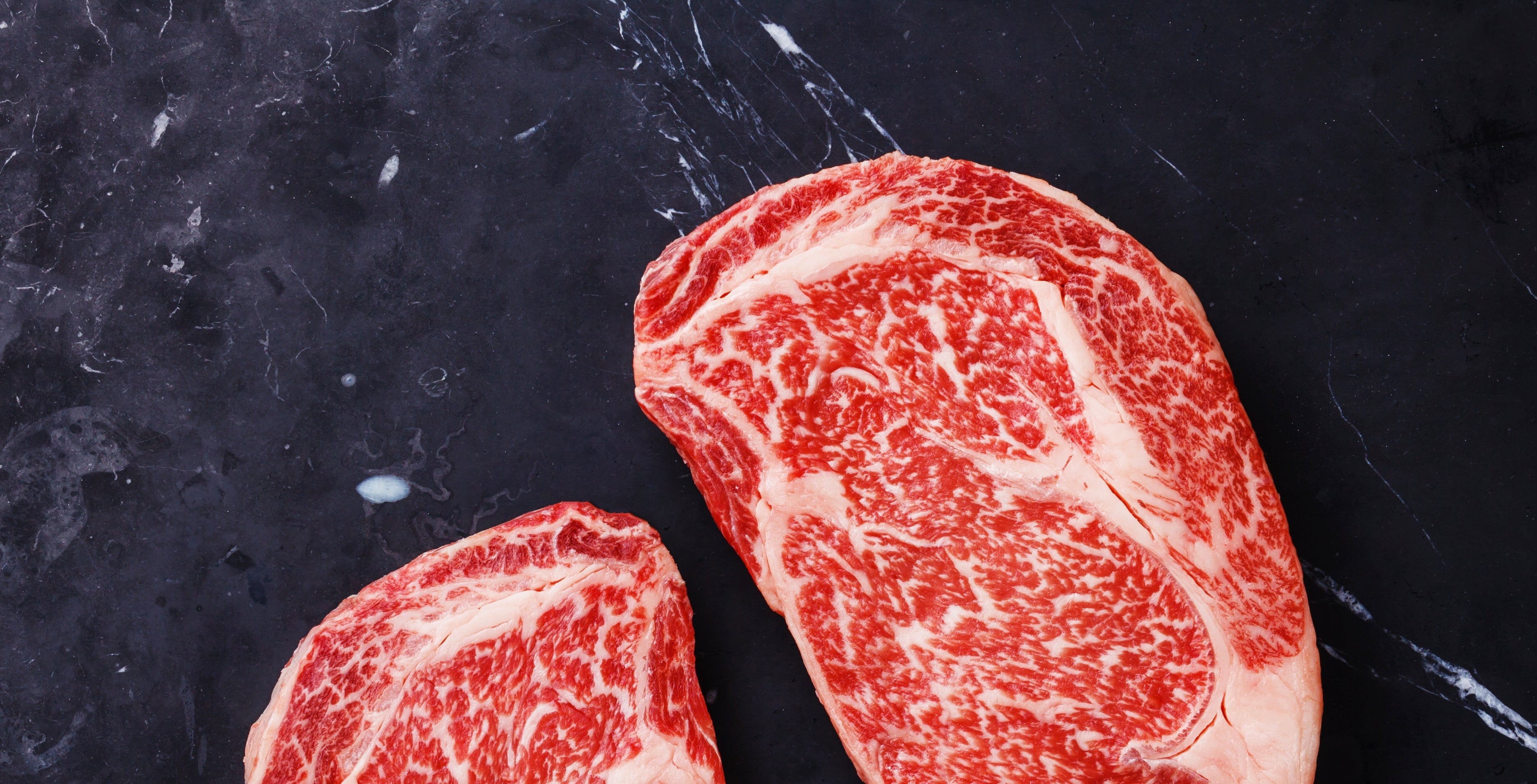 Two marbled raw steaks on a dark surface