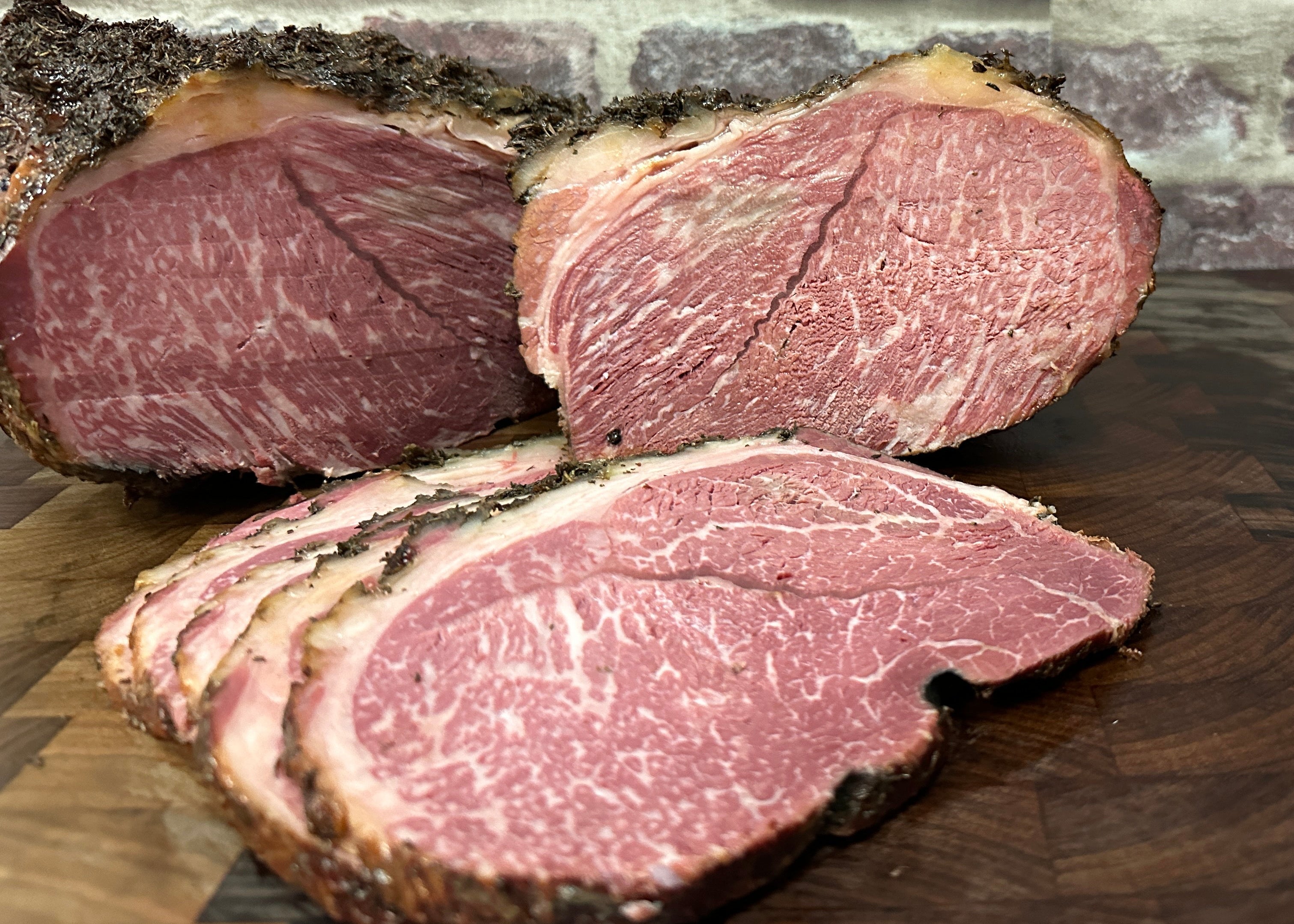 A piece of Wagyu Beef Ham with visible grain fat and connective tissue, placed on a wooden cutting board against a brick wall background.
